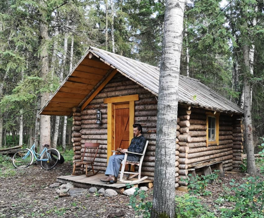 Jake Vaadeland sitting on a rocking chair outside of the cabin he built.