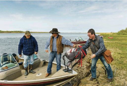Three people unload a motor boat at the Saskatchewan River Delta.