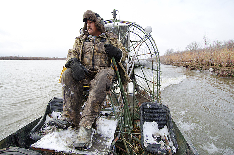 Gary drives airboat near water's edge.